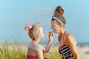 Happy mother and child applying lipstick with spf on seacoast