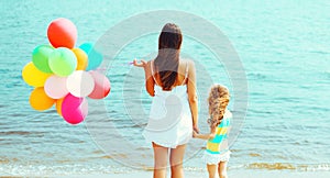 Happy mother and child daughter with colorful balloons on beach near sea, back view