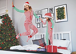 happy mother and child daughter in pajamas jumping in bed on christmas morning .