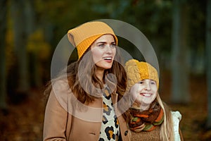 Happy mother and child in hats outside in city park in autumn