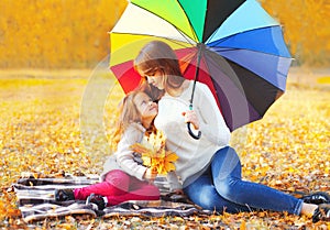 Happy mother and child little girl with umbrella and yellow maple leaves in sunny autumn park