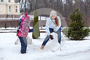 Happy mother with child making snowman with snow in winter park