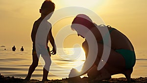 Happy Mother and child playing with sand on the beach against sunset.