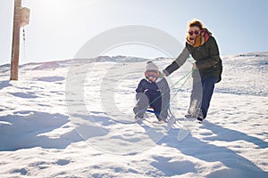 Happy mother and child playing in the snow with a sledge