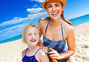 Happy mother and child on seashore applying suntan lotion