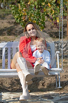 Happy mother and child swinging outdoor. Young mother with little kid son sitting on swing in summer park. Mothers day