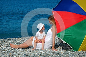 Happy mother with child under umbrella on beach