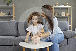 Happy mother and child who plan on saving up some money are putting coins in piggy bank