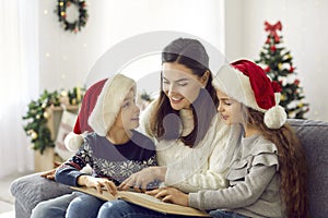 Happy mother and children sitting on couch and reading book on Christmas Eve at home