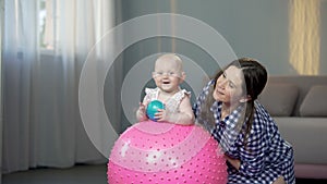 Happy mother and cute baby girl smiling at camera, playing with balls at home