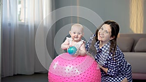 Happy mother and cute baby girl smiling at camera, playing with balls at home