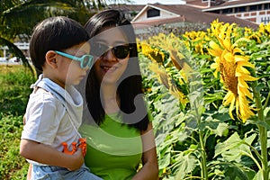 Happy mother and cute boy in sunflower field, outdoor activity of family in the morning