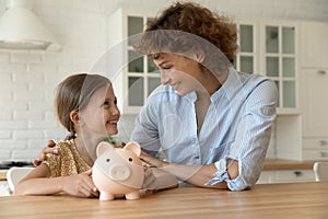 Happy mother and little girl holding piggy bank, saving money
