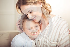 Happy mother and cute little son hugging together at home