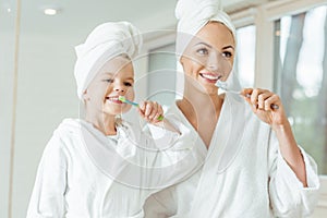 happy mother and daughter in bathrobes and towels brushing photo