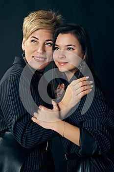 Happy mother and daughter. Beautiful middle-aged woman posing with young girl over dark studio background. Concept of