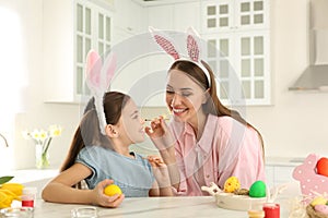 Happy mother and daughter with bunny ears headbands having fun while painting Easter egg