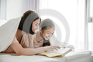 Happy mother and  daughter child reading book together in bed