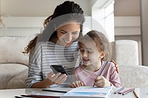 Happy mother with daughter distracted from drawing using smartphone