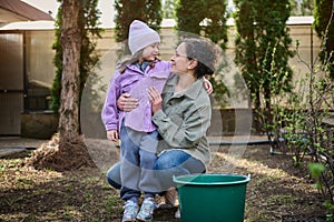 Happy mother and daughter enjoying gardening in the backyard of their country house, watering baby plants in the looseness ground