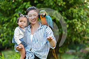 happy mother and daughter feeding blue-and-yellow macaw (Ara ararauna) bird on hand
