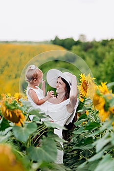 Happy mother with the daughter in the field with sunflowers. mom and baby girl having fun outdoors. family concept