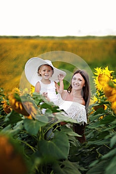 Happy mother with the daughter in the field with sunflowers. mom and baby girl having fun outdoors. family concept