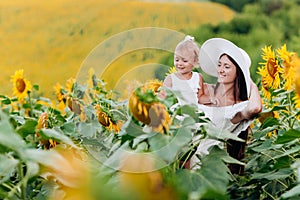 Happy mother with the daughter in the field with sunflowers. mom and baby girl having fun outdoors. family concept