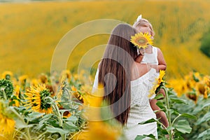 Happy mother with the daughter in the field with sunflowers. mom and baby girl having fun outdoors. family concept