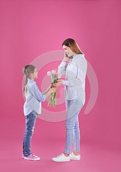 Happy mother and daughter with flowers on color background