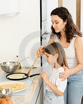 Happy mother and daughter frying pancakes in the kitchen