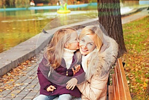 Happy mother with daughter have a rest sitting in autumn park on a bench.