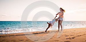 Happy mother and daughter having fun on tropical beach at sunset - Family playing next sea during summer vacation