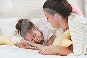 Happy mother and daughter hug and laugh and have fun lying on the bed