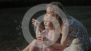 A happy mother and daughter inflate soap bubbles. Family in a city park on a picnic on a warm evening at sunset.