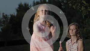 A happy mother and daughter inflate soap bubbles. Family in a city park on a picnic on a warm evening at sunset.