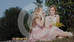 A happy mother and daughter inflate soap bubbles. Family in a city park on a picnic on a warm evening at sunset.