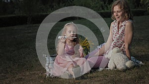 A happy mother and daughter inflate soap bubbles. Family in a city park on a picnic on a warm evening at sunset.