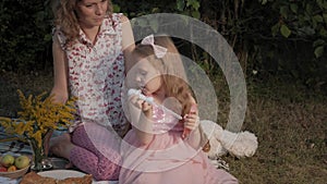 A happy mother and daughter inflate soap bubbles. Family in a city park on a picnic on a warm evening at sunset.