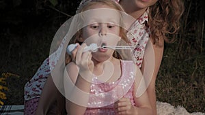 A happy mother and daughter inflate soap bubbles. Family in a city park on a picnic on a warm evening at sunset.