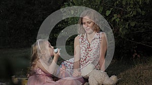 A happy mother and daughter inflate soap bubbles. Family in a city park on a picnic on a warm evening at sunset.