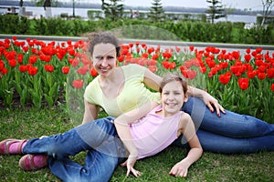 Happy mother and daughter lie on grass near red