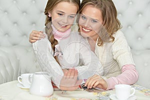 Happy mother and daughter looking at fingernails while reading magazine and drinking tea together