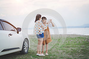 Happy mother and daughter looking smartphone and having fun on a tropical beach and a car on the side. Family vacation holiday and