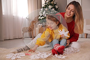 Happy mother and daughter making paper snowflake near Christmas tree at home