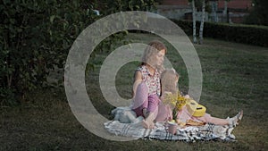 A happy mother and daughter are playing on the ukulele. Family in a city park on a picnic on a warm evening at sunset.