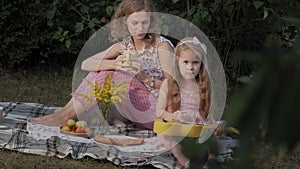 A happy mother and daughter are playing on the ukulele. Family in a city park on a picnic on a warm evening at sunset.