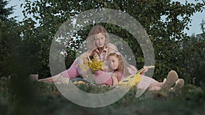 A happy mother and daughter are playing on the ukulele. Family in a city park on a picnic on a warm evening at sunset.