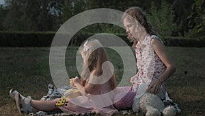 A happy mother and daughter are playing on the ukulele. Family in a city park on a picnic on a warm evening at sunset.