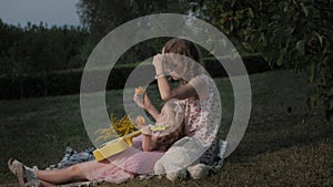 A happy mother and daughter are playing on the ukulele. Family in a city park on a picnic on a warm evening at sunset.